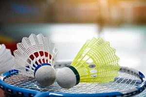 White and yellow plastic badminton shuttlecock and racket with neon light shading on green floor in indoor badminton court, blurred badminton background, copy space. photo