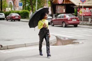 Portrait of young beautiful african american woman holding black umbrella and walking crosswalk. photo