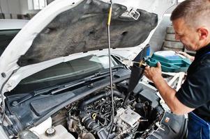 Car repair and maintenance theme. Mechanic in uniform working in auto service, pouring new motor oil.