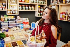 chica de rojo con diferentes productos en la cesta en la tienda de delicatessen. foto