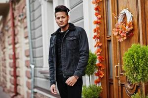 hombre indio guapo y de moda con chaqueta negra de jeans posada al aire libre. foto