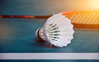 Cream white badminton shuttlecock and racket with neon light shading on green floor in indoor badminton court, blurred badminton background, copy space. photo