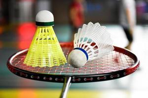 White and yellow plastic badminton shuttlecock and racket with neon light shading on green floor in indoor badminton court, blurred badminton background, copy space. photo