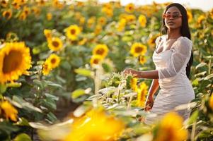 una mujer negra muy joven usa una pose de vestido de verano en un campo de girasoles. foto
