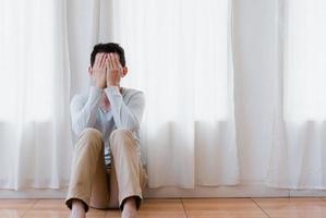 Depressed asian young man covering face by hands, crying alone at home, upset man sitting , feeling unhappy after quarrel or breakup, despair and lonely and panic , psychological problem concept photo