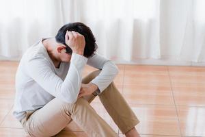 joven asiático deprimido cubriendo la cara con las manos, llorando solo en casa, hombre molesto sentado, sintiéndose infeliz después de una pelea o ruptura, desesperación y soledad y pánico, concepto de problema psicológico foto