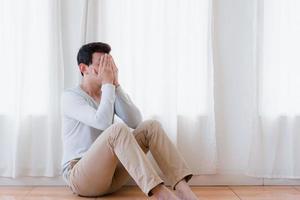 joven asiático deprimido cubriendo la cara con las manos, llorando solo en casa, hombre molesto sentado, sintiéndose infeliz después de una pelea o ruptura, desesperación y soledad y pánico, concepto de problema psicológico foto