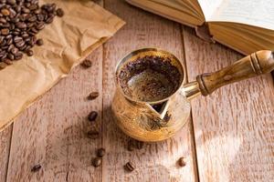 fresh breved coffe in  cezve traditional turkish coffee pot opened book and coffee beans on wooden table. photo