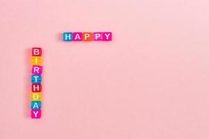 inscripción de feliz cumpleaños hecha de coloridas cuentas de cubo con letras. concepto de fondo rosa festivo con espacio de copia foto