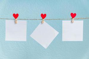 tarjetas en blanco en alfileres con corazones rojos. maqueta para texto y fondo azul para saludos del día de san valentín foto