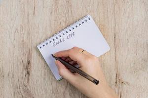 young woman hands hold opened notebook pages with black pen on  wooden table. Goals 2019 list. photo