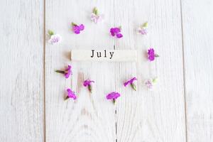 top view of wooden calendar with July sighn and pink flowers. photo