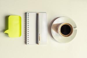 vista superior del bloc de notas en espiral vacío, bolígrafo plateado, pegatina amarilla y taza de café sobre fondo blanco. concepto de negocio o educación foto