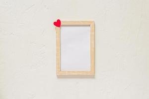 wooden photo frame with red heart on white wall baxkground. Minimal flat lay with copy space