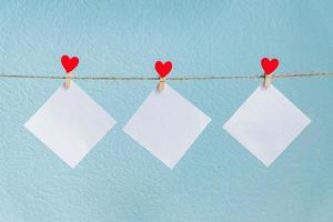 tarjetas en blanco en alfileres con corazones rojos. maqueta para texto y fondo azul para saludos del día de san valentín foto