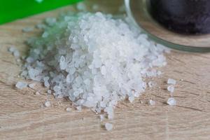 Pile of sea salt and black candle on wooden table. Natural ingredient for spa and exfoliation. photo