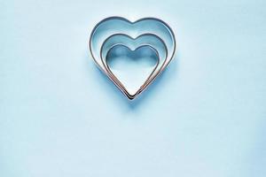 Three metal cookie cutters in heart shape on light blue background with copy space photo