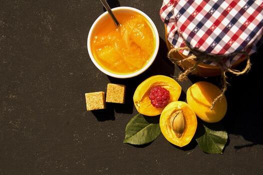 Top view of jar with homemade organic apricot jam and ripe apricots and raspberry on black background. Copy space for your text photo