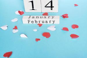 concepto de día de san valentín y vacaciones - calendario de madera de cubo con fecha del 14 de febrero y corazones pequeños de papel cortados en el fondo azul. decoración hecha a mano. foto