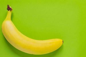 Ripe single banana on bright green background. Minimal flatlay, top view, copy space photo