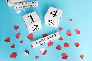 valentines day and holidays concept - cube wooden calendar with 14th february date and cut out paper small hearts on blue backround. Handmade decoration. photo