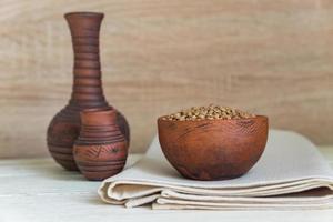 Dry buckwheat in brown clay bowl on wooden table. gluten free grain for healthy diet photo
