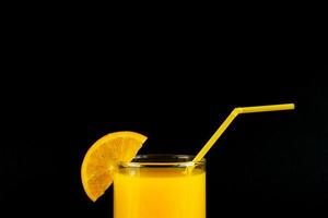 jugo de naranja fresco y saludable en un vaso con una rodaja de cítricos sobre fondo negro. copiar espacio para texto foto