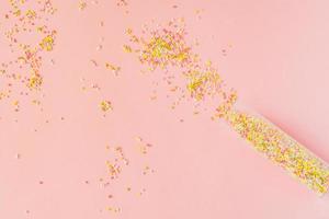 multicolored sugar sprinkles on pink background. Confectionary decorations  spilling out of a plastic bottle photo