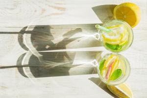 top view of glass of homemade lemonade with lemons, mint and paper straws on wooden rustic background. Summer refreshing beverage. hard shadows photo