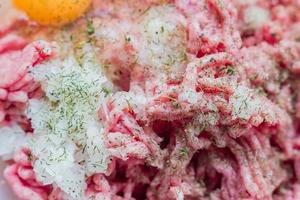 Minced meat in a bowl with raw egg, spices and chopped onion for cooking cutlets, selective focus photo