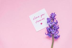 Love you forever paper tag and purple hyacinth flower on wooden table. Top view, miniml flat lay photo