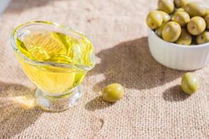 fresh marinated green olives in white ceramic bowl and sauceboat of premium virgin olive oil on burlap cloth background photo