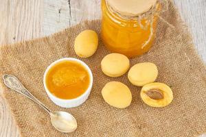 Home made organic apricot jam in glass jar and ripe apricots on wooden rustic table photo