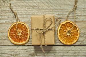 Christmas decor. Dried orange slice and gift box in craft paper on wooden background, top view, minimal flat lay photo