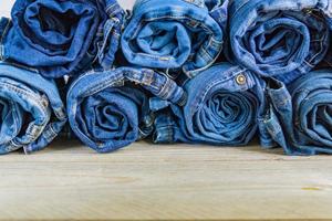 top view of roll blue denim jeans arranged in stack on wooden shelf. Beauty and fashion clothing concept photo