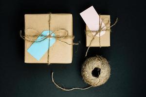 Handcrafted gift box wrapped in Craft paper with red wooden heart, rope and bow on black background. Top view, flat lay photo