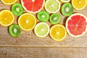 frame with slice of oranges, lemons, kiwi, grapefruit pattern on wooden background. Flat lay, top view with copy space. photo