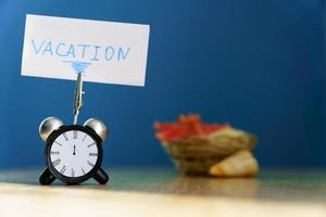 Alarm clock and banner with handwritten phrase vacation on wooden table. Vacation concept. photo