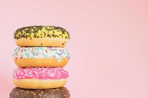 pila de donuts dulces glaseados con chispas y nueces sobre fondo rosa. copia el ritmo de tu texto foto