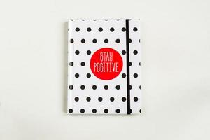 Black and white polka dot note book with red circla and stay positive inscription on the cover. photo