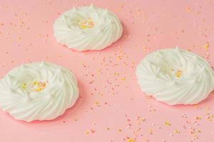 homemade white air meringues and confectionery decorations on pink background photo