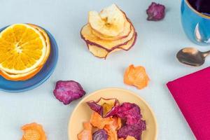 alimentos saludables nutrición orgánica. manzana cortada y seca, naranja, zanahoria y remolacha y taza de té sobre mantel textil. foto