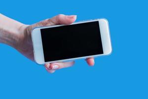 white mobile phone in left female's hand on blue background with copy space photo