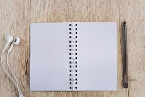 concepto de negocio y oficina: cuaderno en blanco, auriculares y bolígrafo negro sobre una mesa de madera. plano mínimo, vista superior. foto