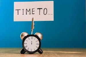 Alarm clock and banner with handwritten phrase time to on wooden table. Time management concept. photo