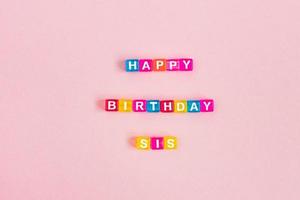 Happy birthday sis inscription made of colorful cube beads with letters. Festive pink background concept with copy space photo