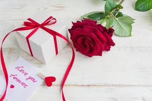 Beige polka dot gift box with red ribbon bow and bautiful red roses on wooden background. Greeting card for holiday. photo