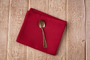 Top view of cloth napkin of red color and served tea spoon on wooden table. photo