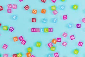 Multicolored plastic cube beads with letters scattered on blue background and words hello. English Alphabet background texture photo