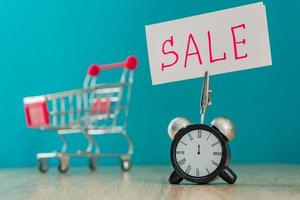 Alarm clock and banner with handwritten world SALE on wooden table. Shopping concept. photo